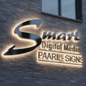 Illuminated 3D signage for Smart Digital Media PAARL - SIGNS, featuring the large glowing logo with backlit lettering mounted on a modern brick building wall at dusk.