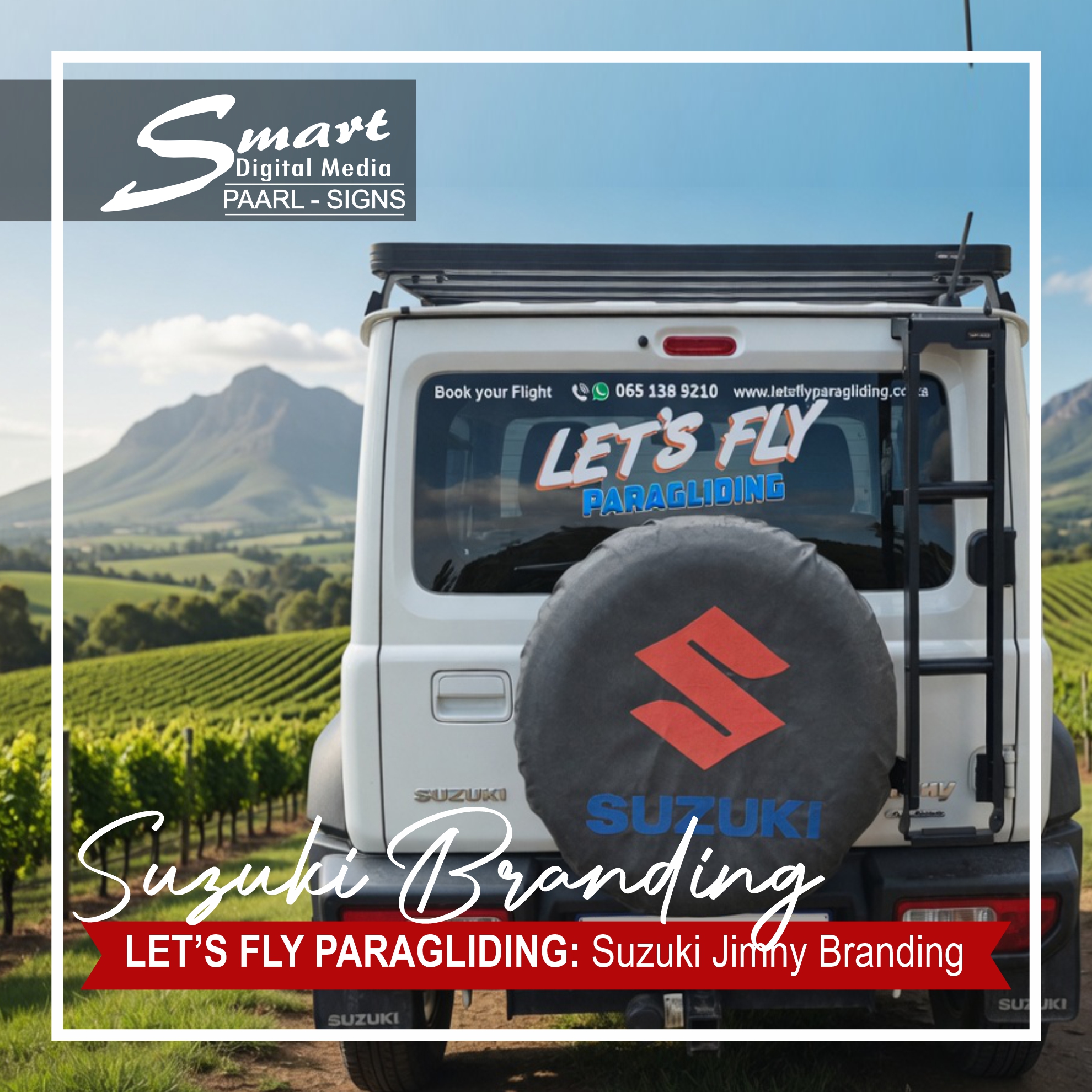 Rear view of a professionally vinyl-branded white Suzuki Jimny for Let's Fly Paragliding by Smart Digital Media Paarl. Features bold “LET’S FLY PARAGLIDING” signage, contact information on the rear window, and Suzuki logo on the spare tire cover, parked on a bright brick-paved street.