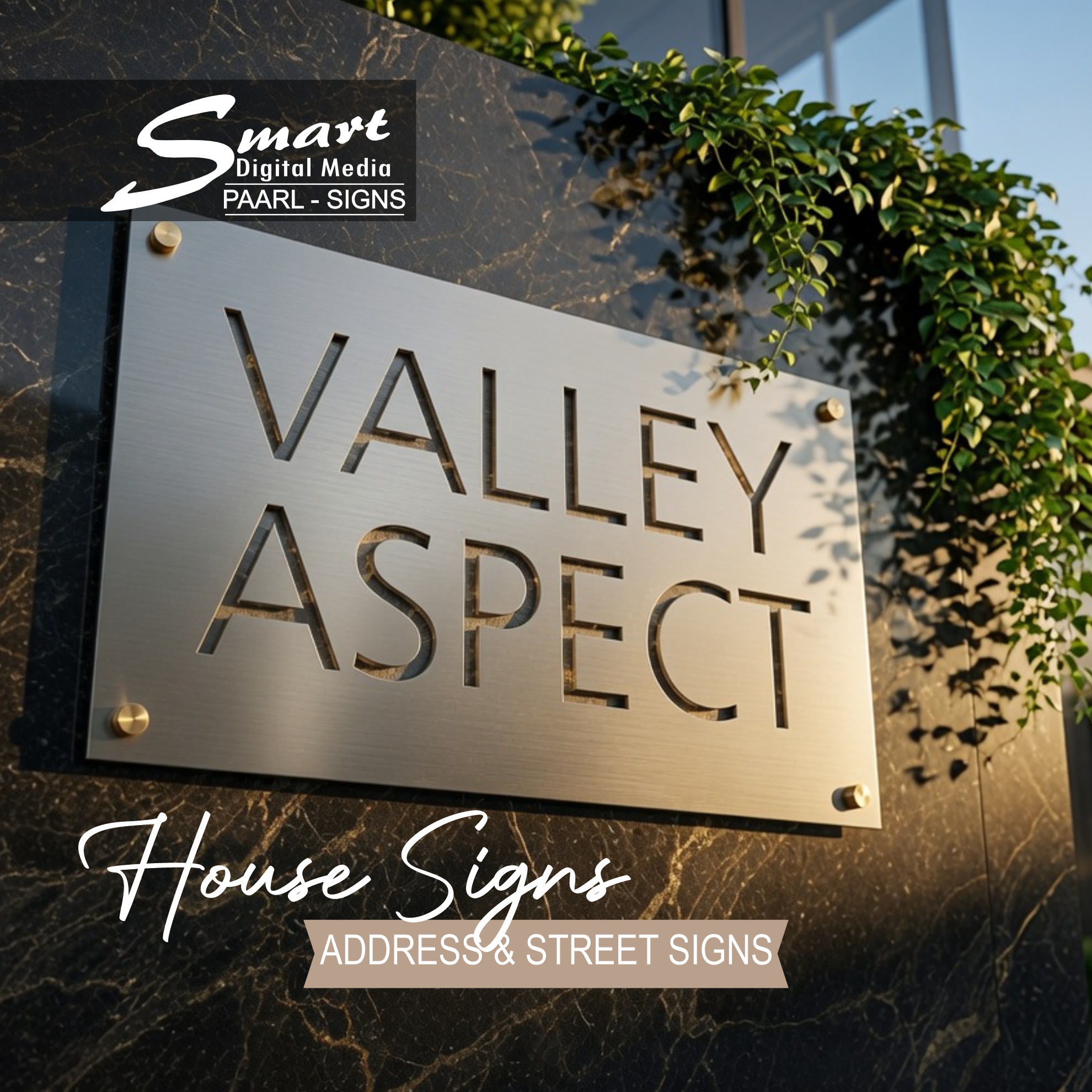 Luxury brushed stainless steel laser-cut address sign reading "VALLEY ASPECT" mounted on a dark marble wall with greenery, showcasing premium metal signage by Smart Digital Media Paarl.